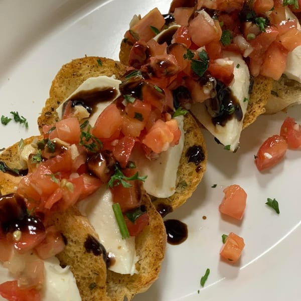 Close-up of Italian bruschetta with diced tomatoes, mozzarella, and balsamic glaze on toasted bread.