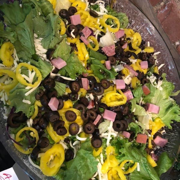 A large Italian salad with lettuce, olives, banana peppers, cheese, and cubed ham.