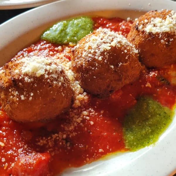 Three golden-brown arancini balls with grated cheese, served on a bed of red marinara sauce and green pesto.