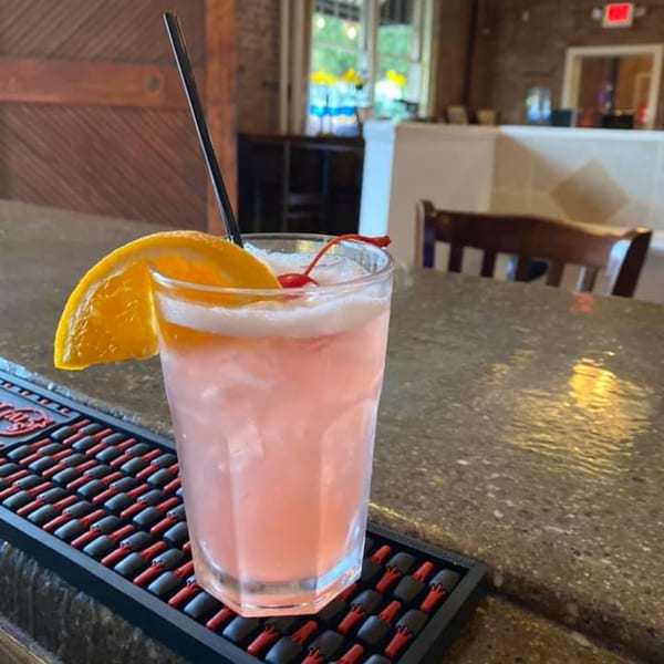 Pink cocktail with an orange slice and cherry on a bar mat at Sainato's at Rivergate.