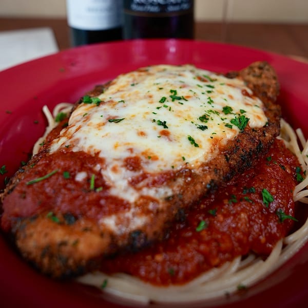 Chicken parmesan with melted cheese and red sauce over spaghetti, served on a red plate.