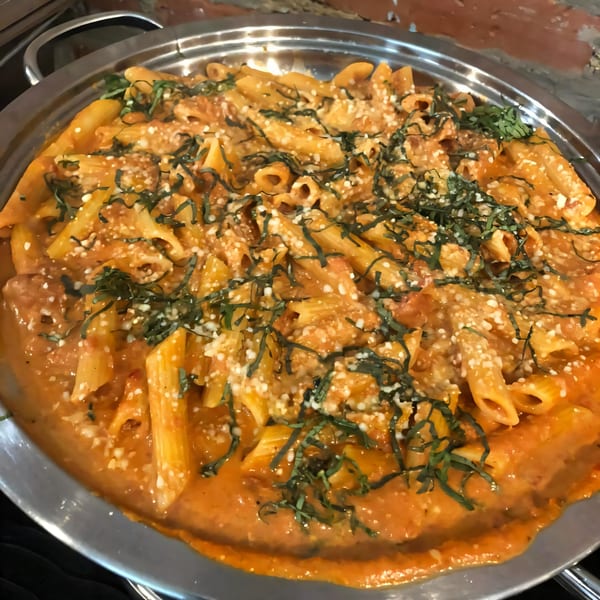Penne pasta in a creamy tomato sauce, topped with grated cheese and fresh basil, served in a metal dish.